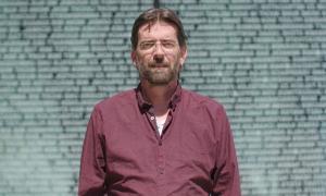 Ein Mann mit dunkelrotem Hemd blickt in die Kamera