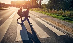 Kinder gehen mit Schulranzen über eine Straße