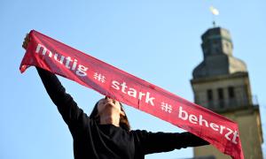 Eine Frau hält ein Banner hoch mit der Aufschrift "mutig, stark, beherzt"