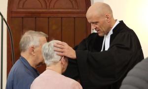 Ein Pfarrer legt seine Hände segnend auf die Köpfe von Gottesdienstbesucherinnen