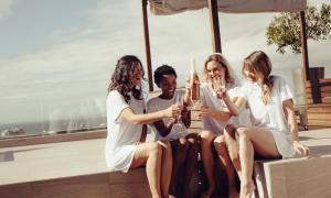 Vier Frauen sitzen in weißen Kleidern zusammen, eine hält eine Sektflasche hoch