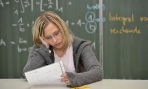 Eine junge Frau sitzt mit einem Blatt vor einer Schultafel