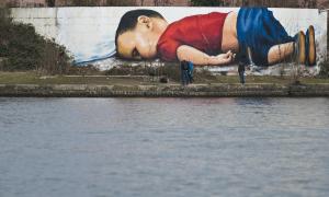 Graffiti an einer 120 Quadratmeter großen Wand in Frankfurt: Der dreijährige Aylan Kurdi liegt tot bäuchlings am Strand, bekleidet mit rotem T-Shirt, blauer Hose und Schuhen.