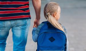 Ein kleines Mädchen mit Rucksack an der Hand eines Mannes
