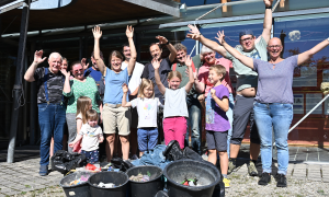 Das Cleanup-Team steht vor den Eimern gesammeltem Müll und streckt glücklich die Arme in die Höhe