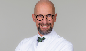 Porträt von Jürgen Herzog, , Ärztlicher Direktor in der Schön Klinik München Schwabing mit schwarzer Brille und Bart.