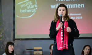 Luisa Neubauer auf dem Podum beim Evangelischen Kirchentag in Hannover mit dem Kirchentagsschal um den Hals und Mikrophon in der Hand