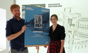 Jonathan Coenen und Rhiannon Moutafis (r.) halten eine Biografie-Tafel in der Hand