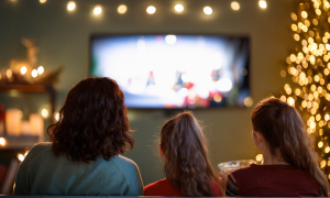 Fernsehr mit Lichterkette drum herum und drei Menschen von hinten, die auf den Fernseher schauen