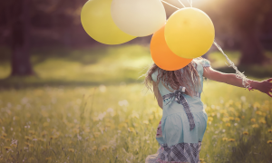 Kind hat Luftballons in de rHand und läuft über eine Wiese