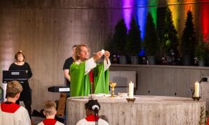 Ein Pfarrer in einem grünen Talar am Altar, um ihn herum Kinder