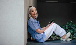 Alte Frau sitzt auf Mauer mit Handy in der Hand