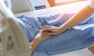 eine Frau hält den Arm einer Person, die im Krankenhaus liegt