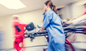 In der Notaufnahme wird ein Bett mit Sanitäter:innen und einer Ärztin durch den Gang geschoben.