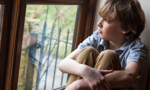 Ein Junge sitzt eingekauert am Fenster und schaut raus