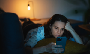 Frau schaut müde aufs Handy und liegt im Bett