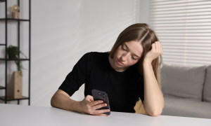 eine junge Frau schaut bedrückt auf ihr Smartphone