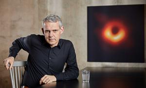 Astrophysiker Heino Falcke sitzt vor einem Bild, wo das schwarze Loch zu sehen ist