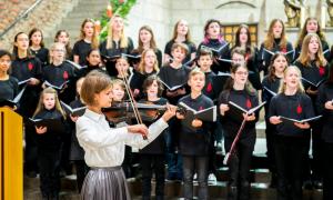 Im Vordergrund steht eine junge Violinistin, im Hintergrund steht ein Schulchor.