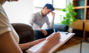 Therapiestunde. Die Therapeutin notiert etwas, der Klient stützt seinen Kopf auf die Hand