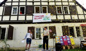 Das Haus „Regen406“  von außen, davor eine Bühne und die künftigen Bewohner, Lorenz Herrmann (li) und Jana Stadler und über ihnenKonfettieregen