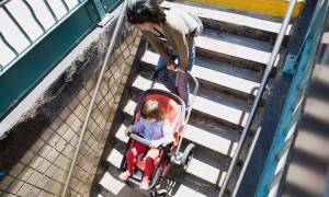 Frau hieft Kinderwagen die Treppe runter