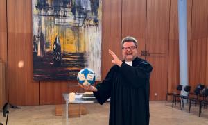 Ein Pfarrer hält einen Fußball und lacht
