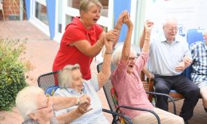 Vier ältere Menschen sitzen auf Stühlen, eine Frau steht dahinter